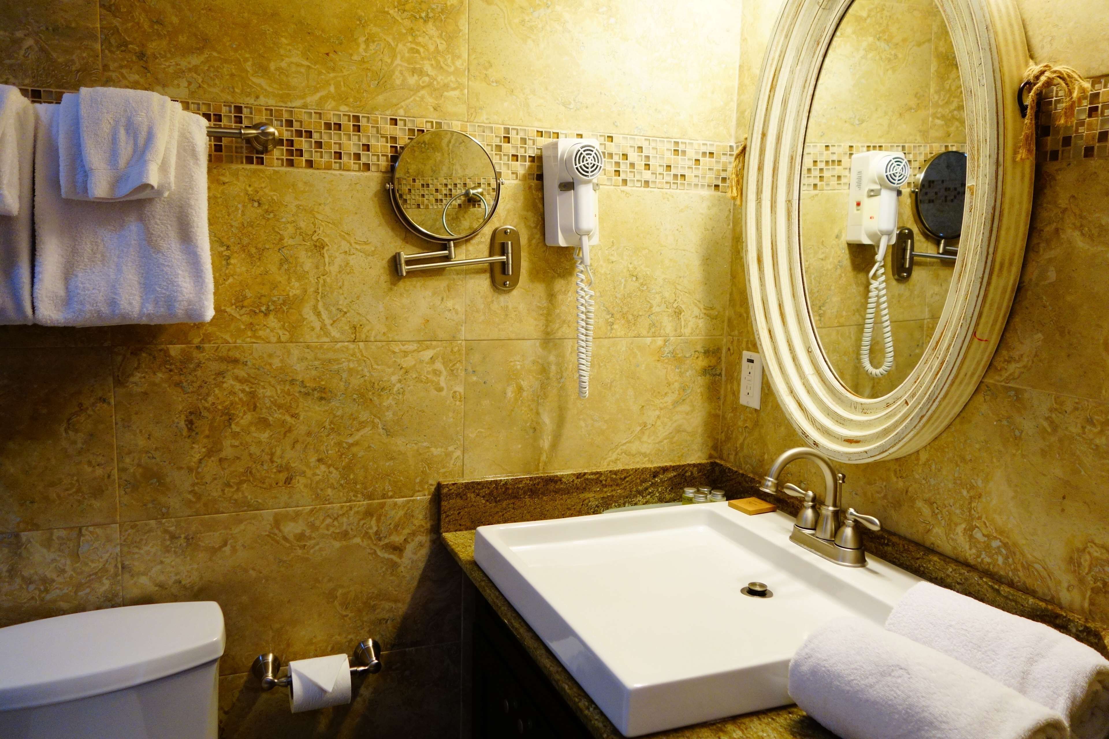 Un baño con lavamanos blanco, espejo, secador de pelo y toallero.