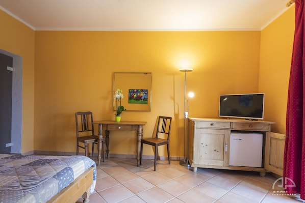 Una habitación con cama, escritorio y silla, televisión, armario y un cuadro en la pared.