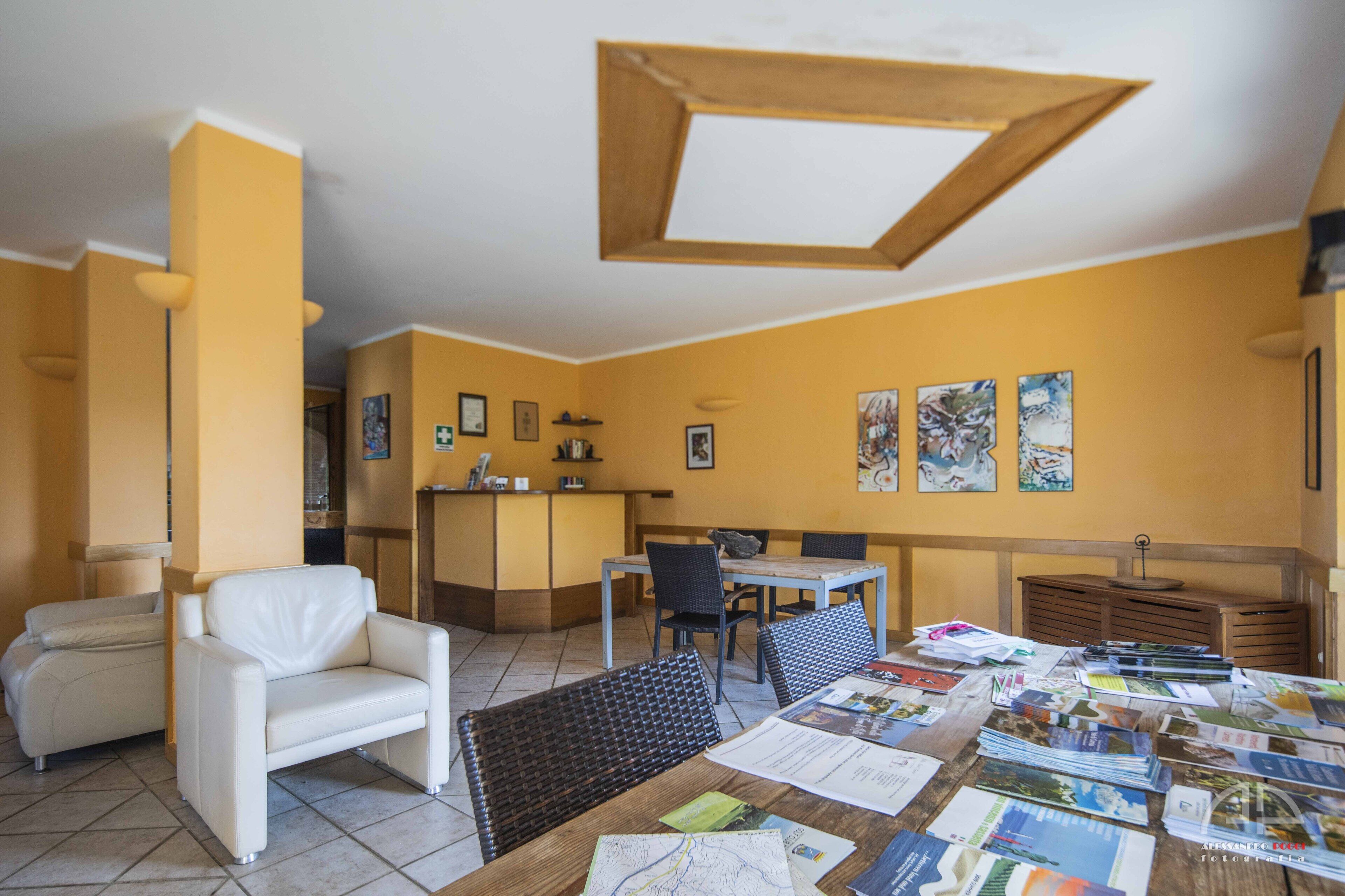 Zona pranzo con tavolo in legno, sedie e diverse brochure.