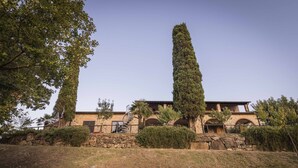 Un bâtiment en pierre avec un escalier menant à un étage supérieur, entouré d’arbres et d’une zone herbeuse.