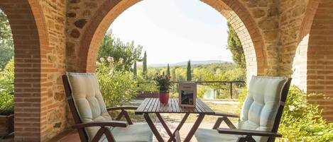 Un patio al aire libre con arcos de piedra, una mesa de madera y dos sillones acolchados.