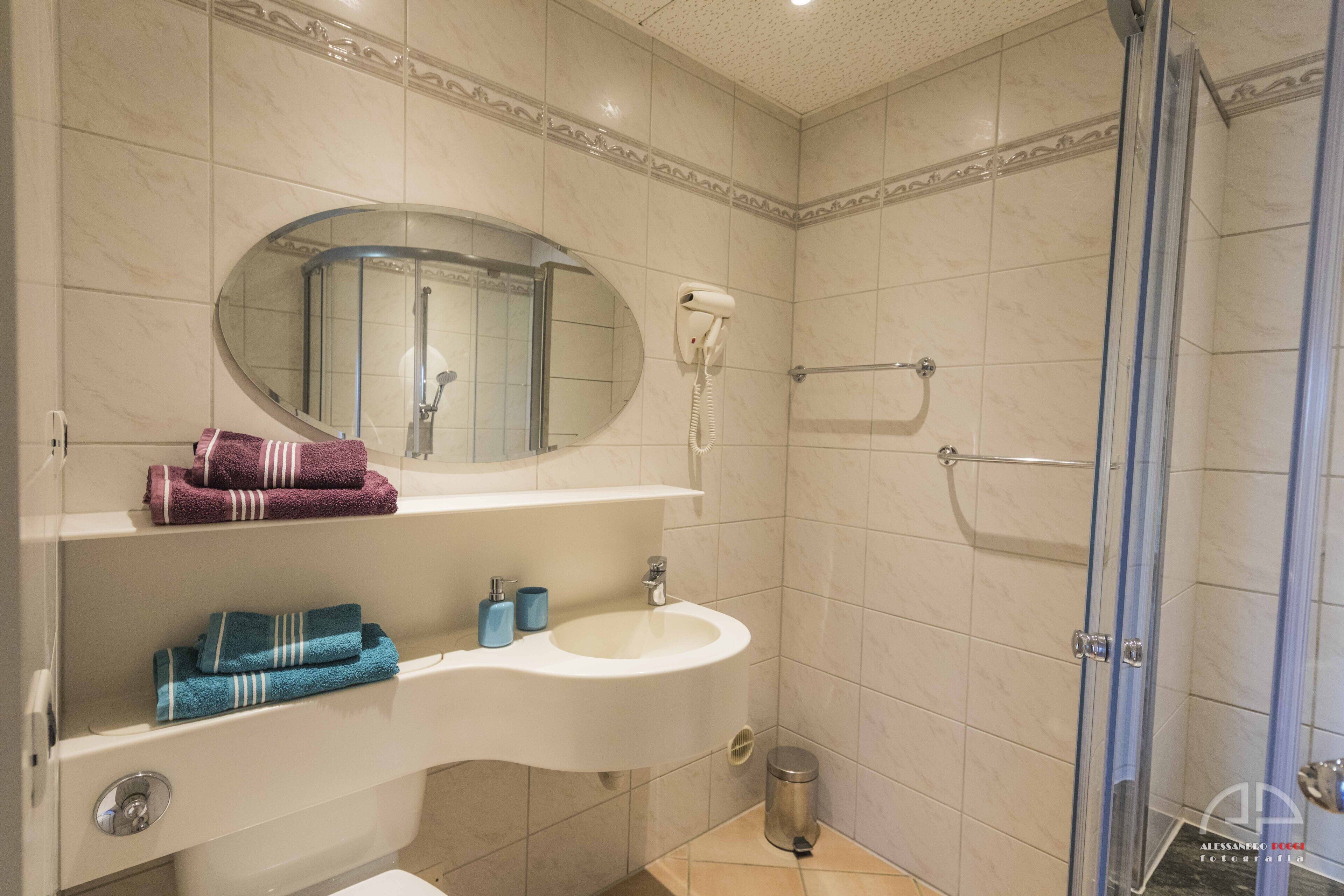 A bathroom with a sink, mirror, towel rack, and shower.