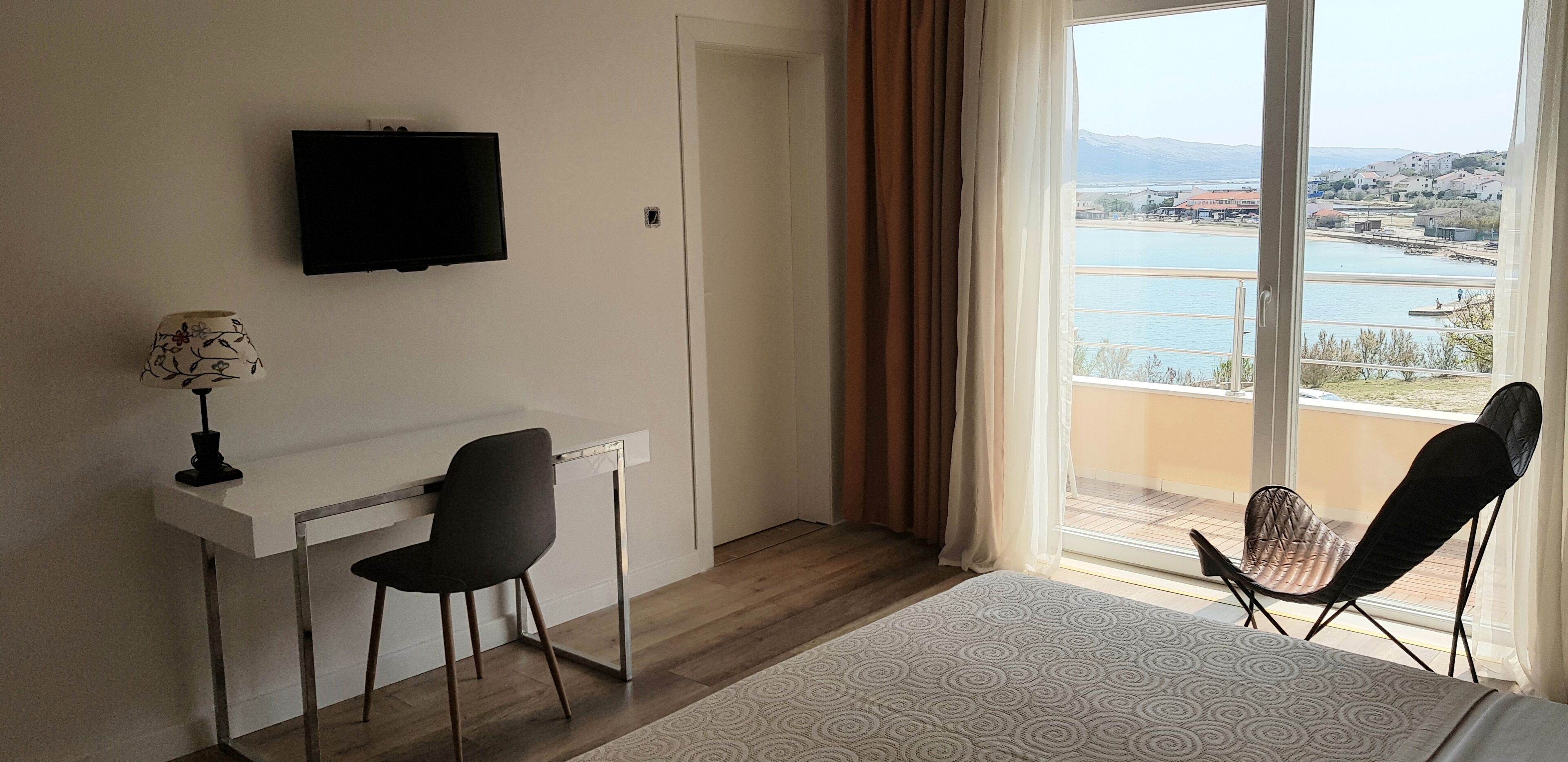 A hotel room with a bed, a desk with a chair, a TV, and a view of a body of water and buildings.