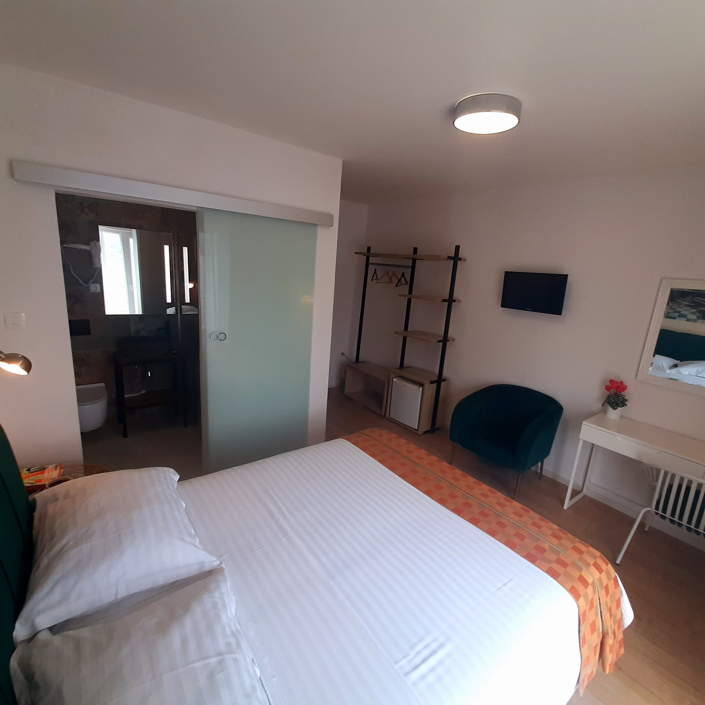 Una habitación de hotel con cama, escritorio, silla, televisor y armario.