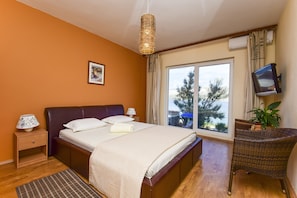 A bedroom with a bed, bedside tables, a television, a window with a view, and a plant. - Guest house Revelin (Pag)