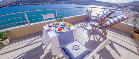 A balcony with a table set for breakfast, overlooking a coastal view.
