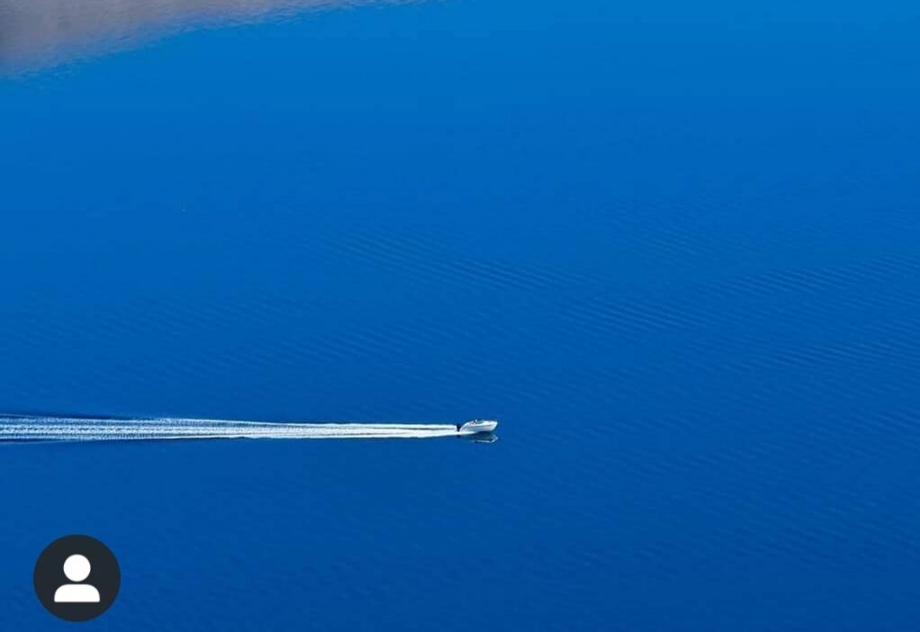 A boat moving across a calm blue body of water.