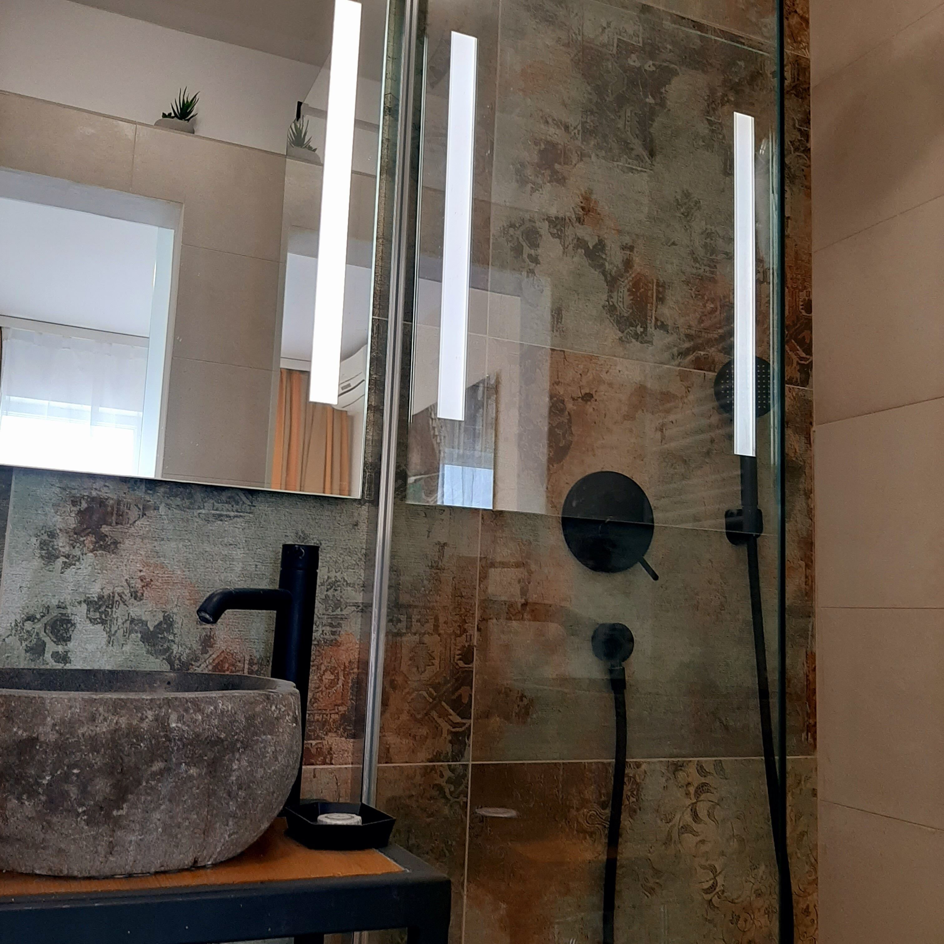 Casa de banho com lavatório de pedra, cabine de duche em vidro e espelho a refletir o espaço.