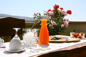 A table with a glass pitcher of orange juice, a glass of water, a white teacup, and a plate of food. - Guest house Revelin (Pag)