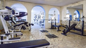 Uma academia com diversos equipamentos de exercício, incluindo aparelhos de musculação e bancos, e piso de ladrilho.