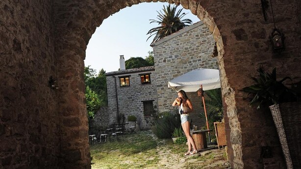 Un arco de piedra conduce a un patio con un edificio de piedra, asientos al aire libre y una persona de pie bajo el arco.