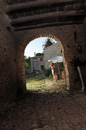 An arched stone doorway leading to a courtyard with a stone building, outdoor seating, and a person standing under the arch. - Antica Locanda Lunetta (Mandas)