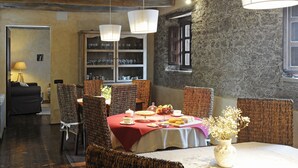 Un comedor con una mesa lista para una comida, rodeado de sillas de mimbre y un aparador con cristalería.