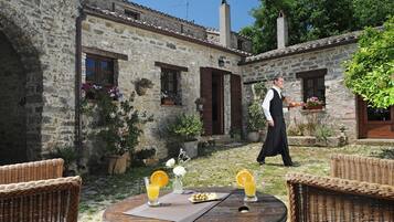 A stone building with a rustic exterior, outdoor seating with wicker furniture, and a table with drinks and snacks.