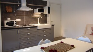Cocina compacta con microondas, estufa, lavabo y armarios. Hay una mesa con un mantel individual y rosas.