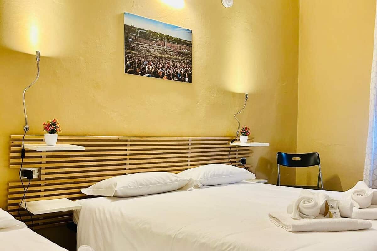 A hotel room with two beds, a wooden headboard, a wall-mounted picture, and a chair.