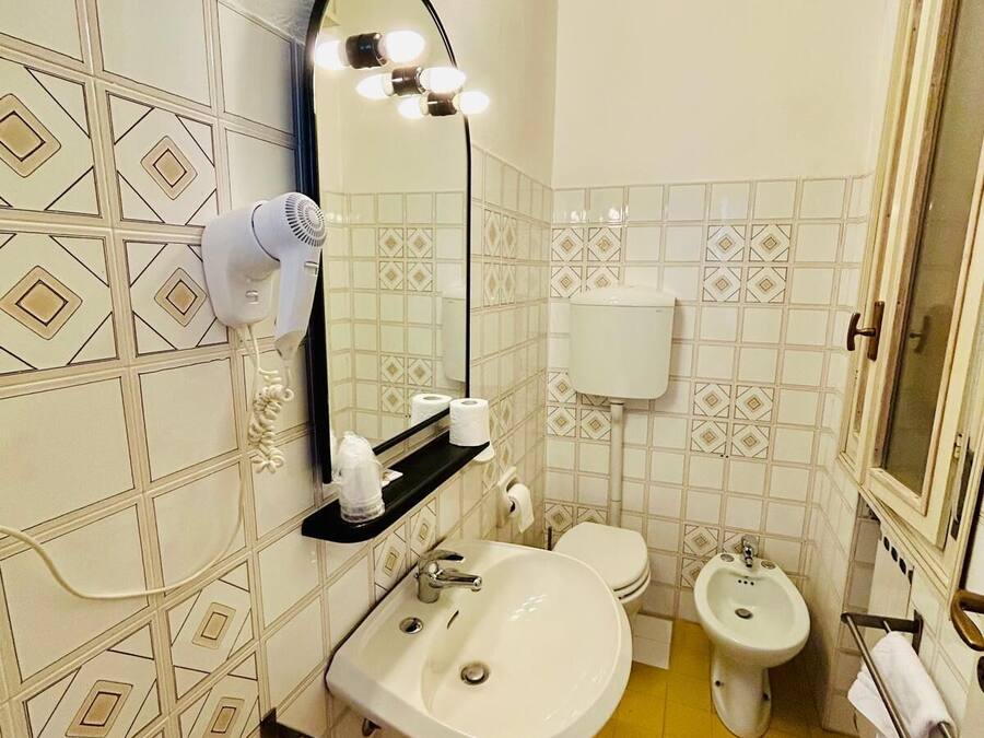 Un baño con lavamanos, espejo, secador de pelo, inodoro, bidé y un perchero para toallas.