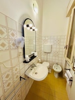 A bathroom with a sink, mirror, hairdryer, toilet, bidet, and a towel rack.