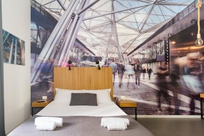A hotel room with a large bed, a wooden headboard, and a view of a busy train station through a large window. - Maison du La Metro (Naples)