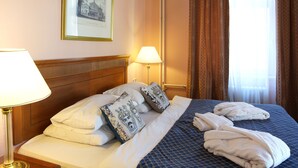 A hotel room with a neatly made bed, two bedside lamps, a framed picture on the wall, and a window with curtains. - Villa Lauretta (Karlovy Vary)