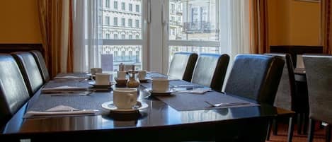 A conference room with a long table, chairs, and a view of buildings through large windows.