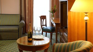 A hotel room with a striped sofa, a dining table with a bottle of champagne and glasses, a wooden chair, and a lamp. - Villa Lauretta (Karlovy Vary)