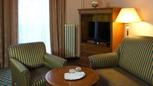 A hotel room with striped armchairs, a wooden cabinet with a television, a table with a tray of glasses, and a lamp. - Villa Lauretta (Karlovy Vary)