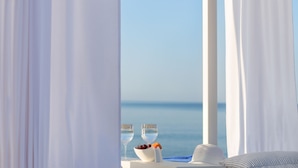 A seaside view with a table set for two, including a bowl of fruit and two glasses of water, and a white hat on the table.