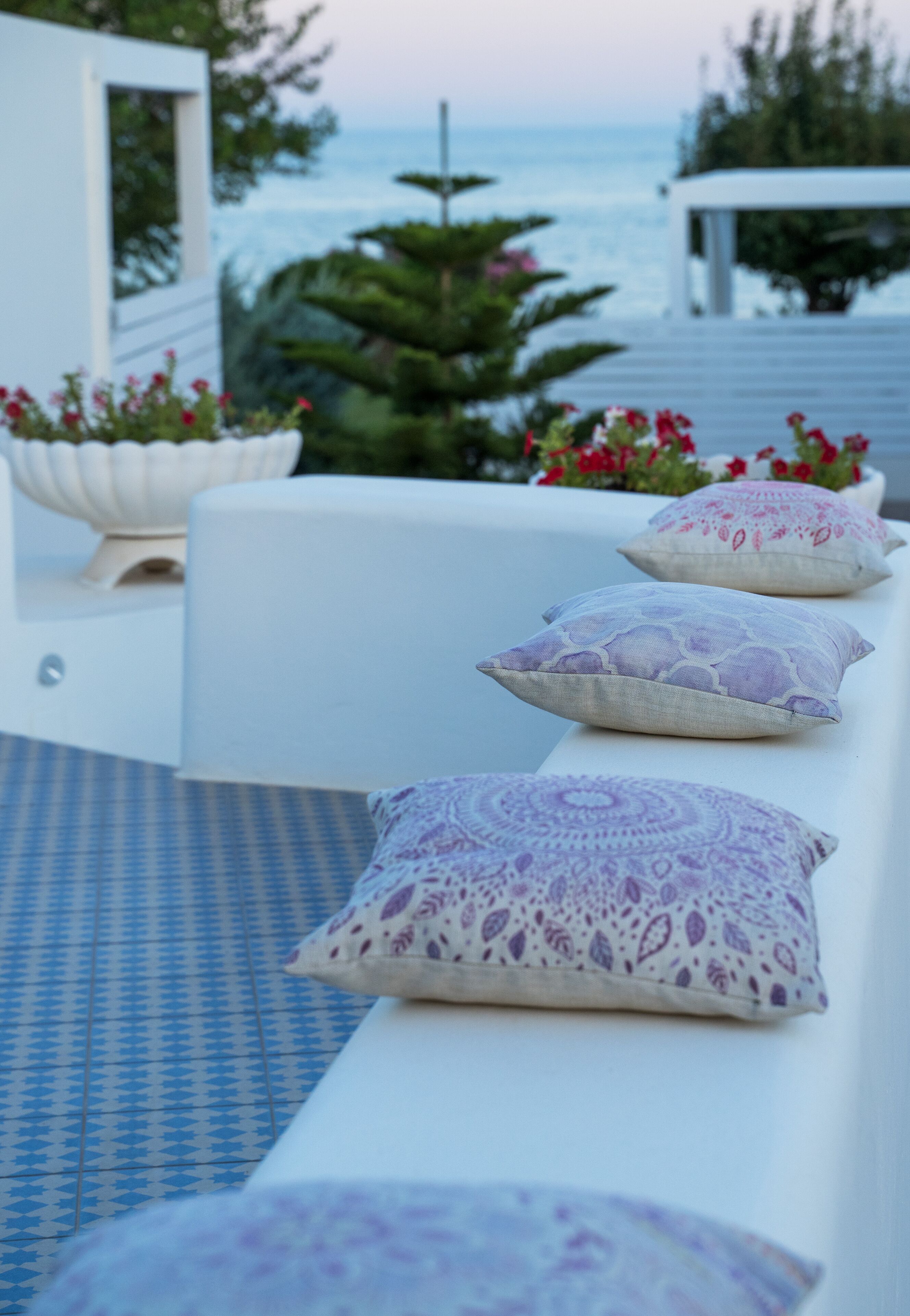 Un área de estar moderna al aire libre con cojines estampados, piso de baldosas y vista al océano.