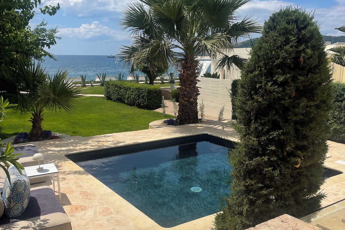 Une piscine dotée d’une plage en pierre, entourée de verdure et offrant une vue sur la mer.