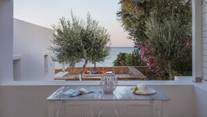 A balcony with a table, chairs, a vase, and a view of the sea and garden.