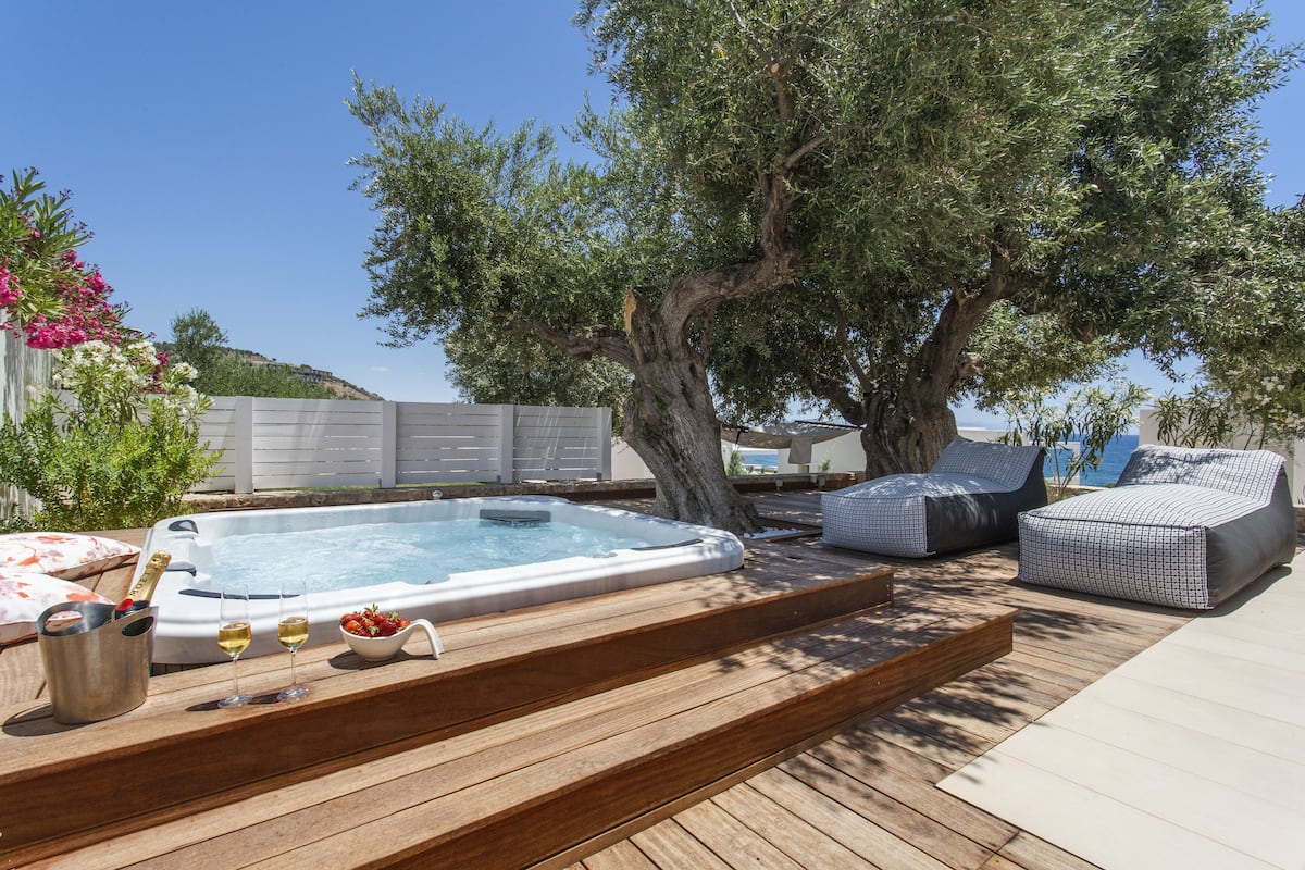 Un bain à remous avec une terrasse en bois, deux chaises longues et un arbre.