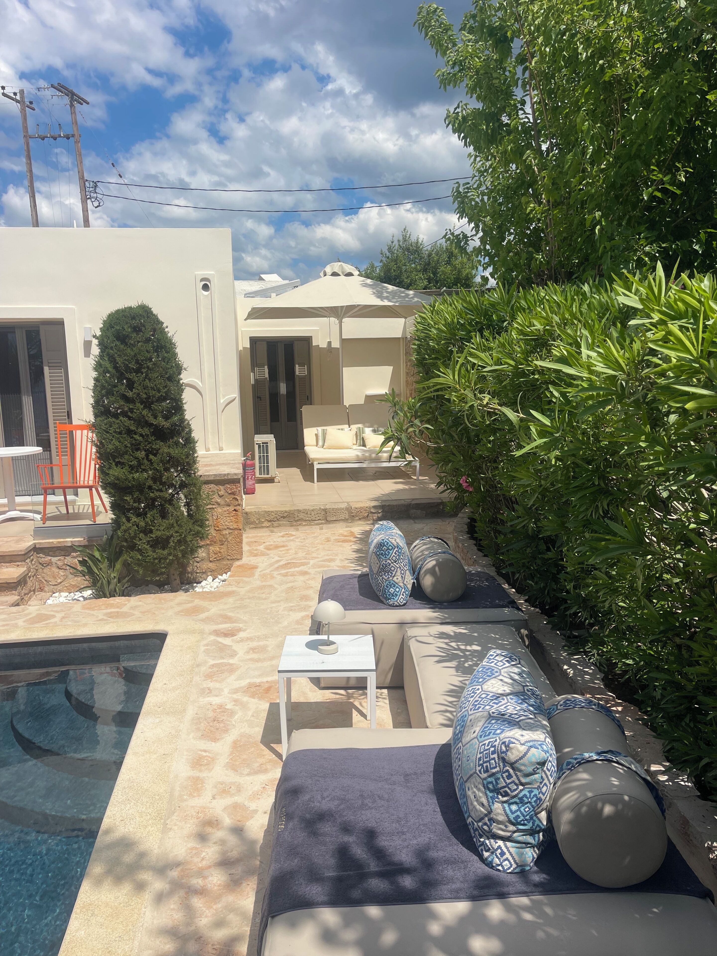 Un área junto a la piscina con una tumbona, una mesita y una zona de estar techada.