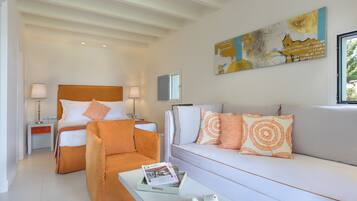 A modern hotel room with a bed, a sofa, a chair, and a coffee table. There is a painting on the wall and a window providing natural light.