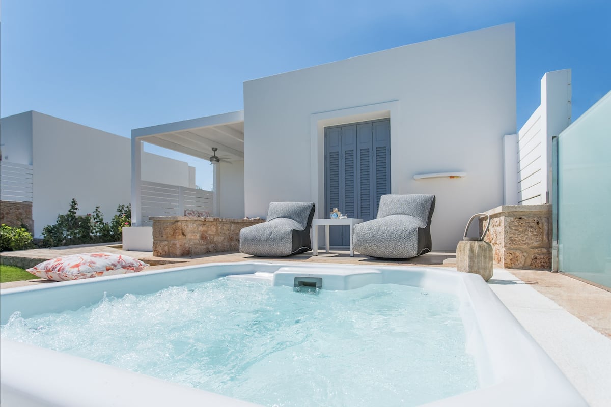 Un espace piscine extérieur moderne, comprenant deux chaises longues, une petite table et un mur en pierre.