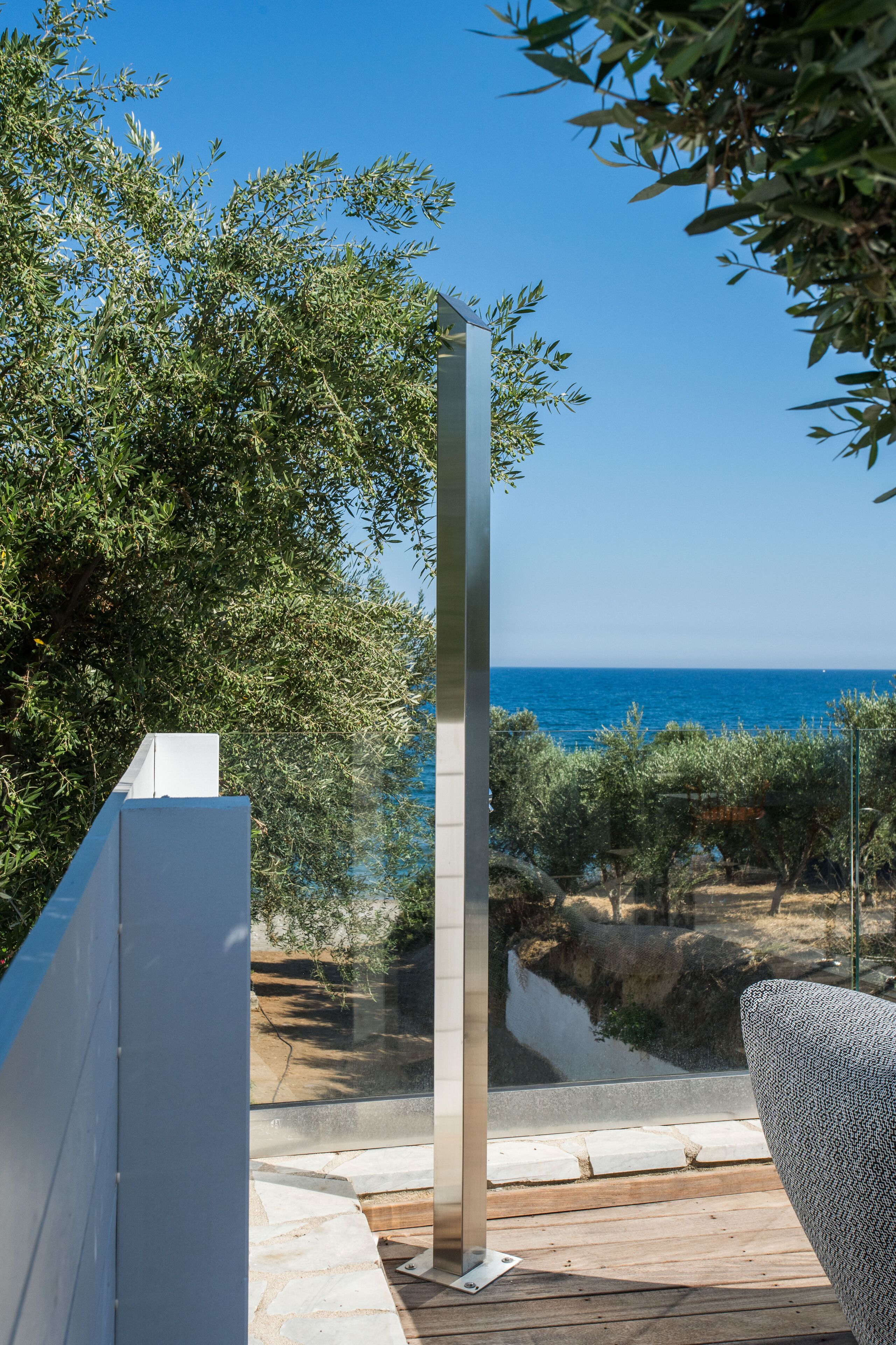 Un balcón con vistas al mar, un alto pilar blanco y una silla con estampado.