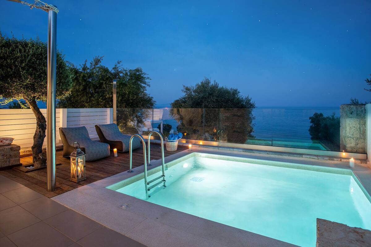 Une piscine avec vue sur la mer, entourée de chaises longues et d’une terrasse en bois.