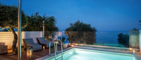 Une piscine avec vue sur la mer, entourée de chaises longues et d’une terrasse en bois.
