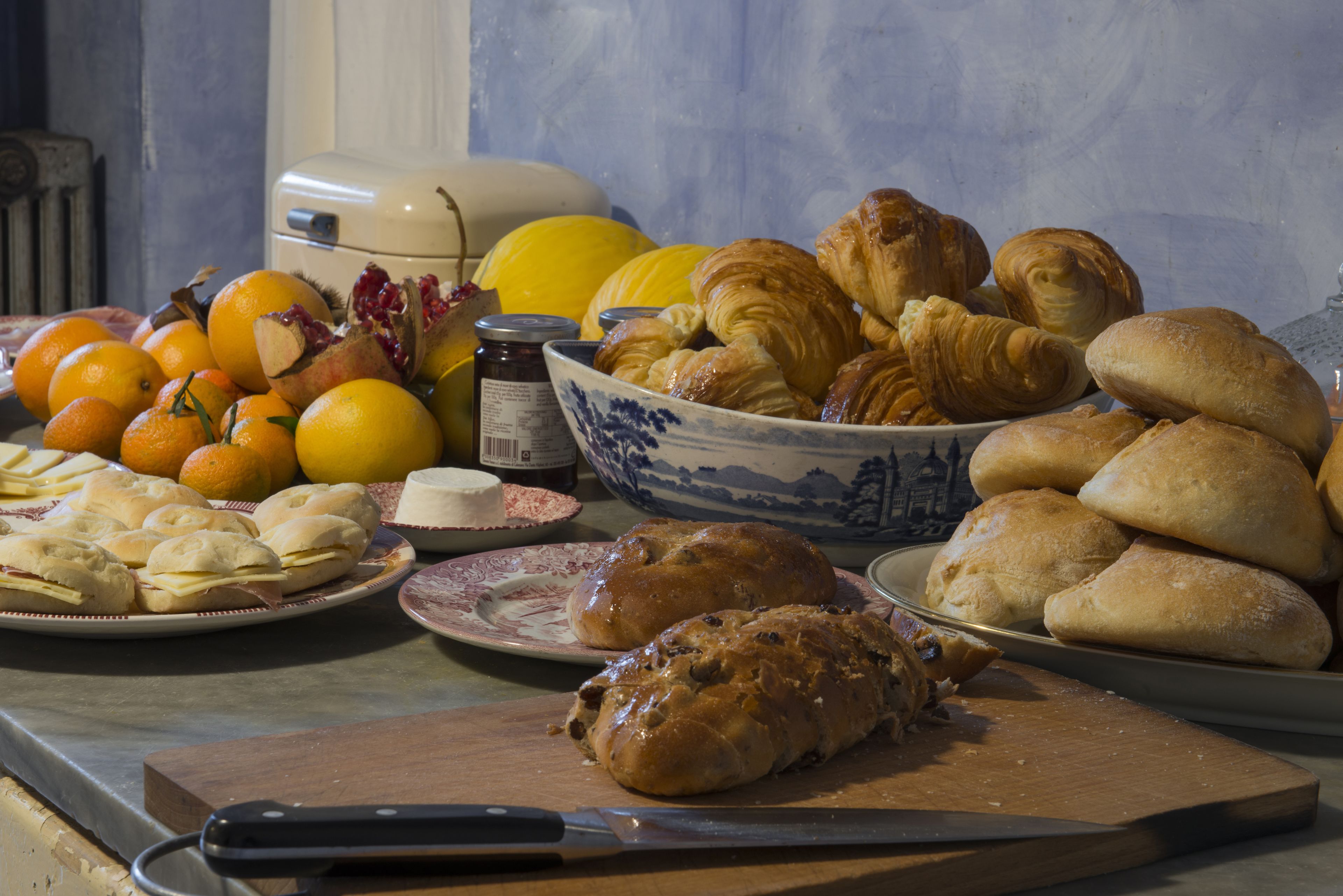 A table with various baked goods, including bread and pastries, and fresh fruits like oranges and a pumpkin.