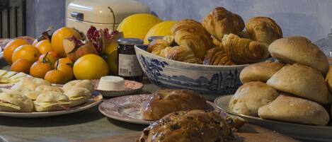 A table with various baked goods, including bread and pastries, and fresh fruits like oranges and a pumpkin.