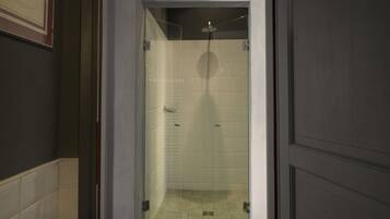A glass-enclosed shower with a handheld showerhead, tiled walls, and a visible drain.