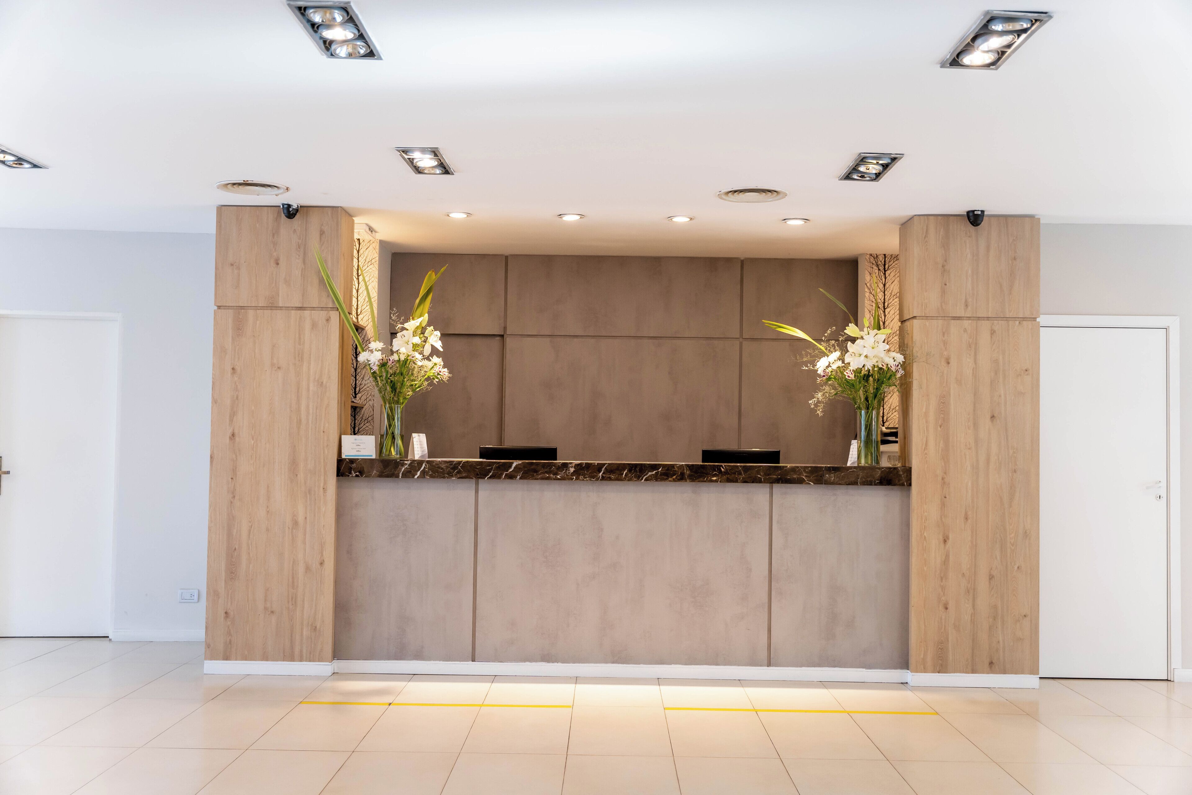 A reception desk with a wooden finish, two flower arrangements, and recessed ceiling lights.