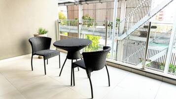 Un balcon avec deux fauteuils en osier et une petite table, une plante en pot, et une vue sur un escalier et la verdure à l’extérieur.