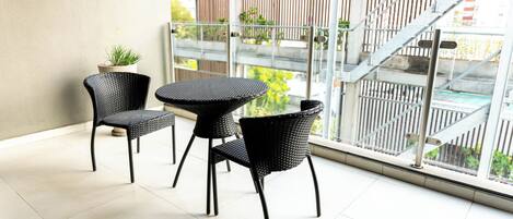 A balcony with two wicker chairs and a small table, a potted plant, and a view of a staircase and greenery outside.