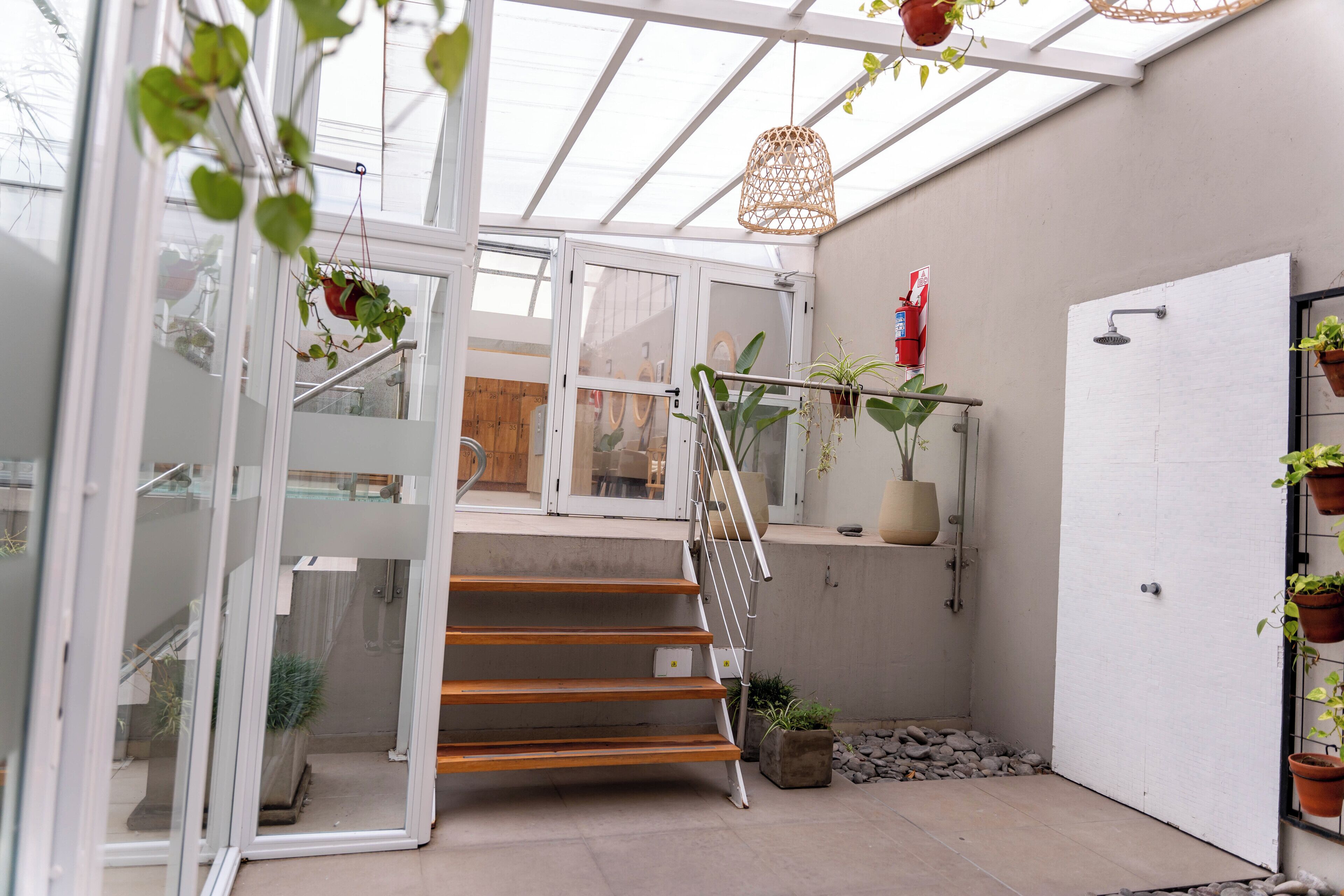 A glass-enclosed staircase with wooden steps and metal railings, leading to a room with a white door and potted plants.