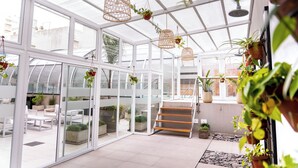 A modern indoor garden with glass walls, wooden furniture, and hanging planters. - O2 Hoteles Mar del Plata (Mar del Plata)