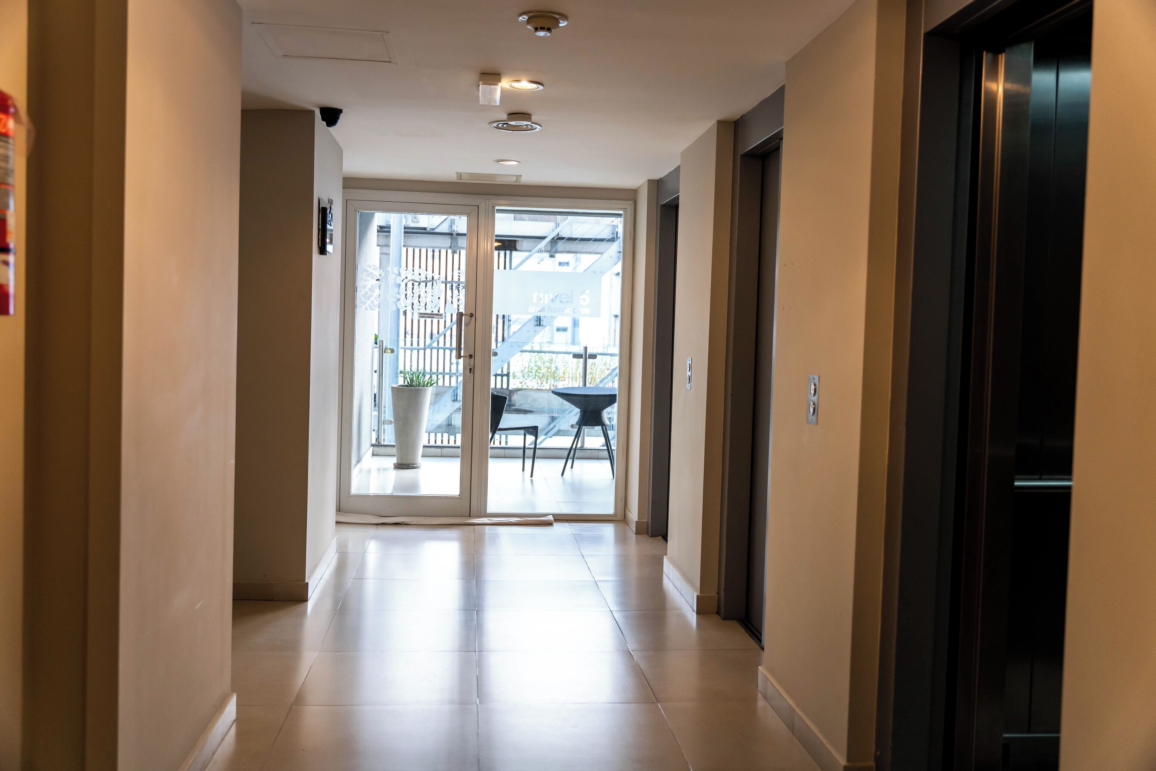 A hallway leading to a glass door with a view of outdoor furniture and a staircase.