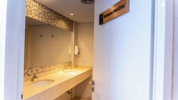 A bathroom with a double sink, a mirror, and a wooden sign above the door.