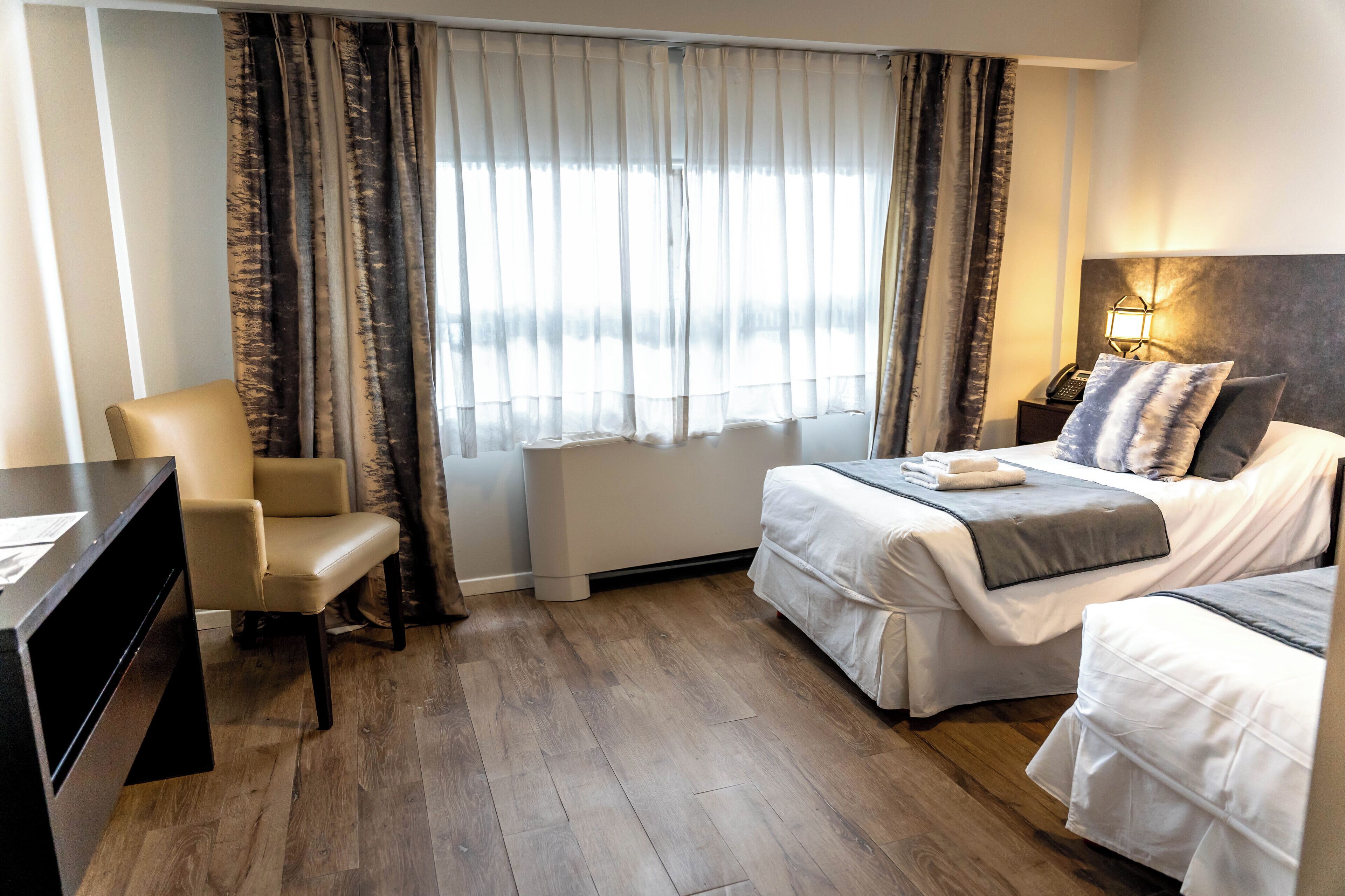 A hotel room with a bed, a chair, a desk, and a window with curtains.