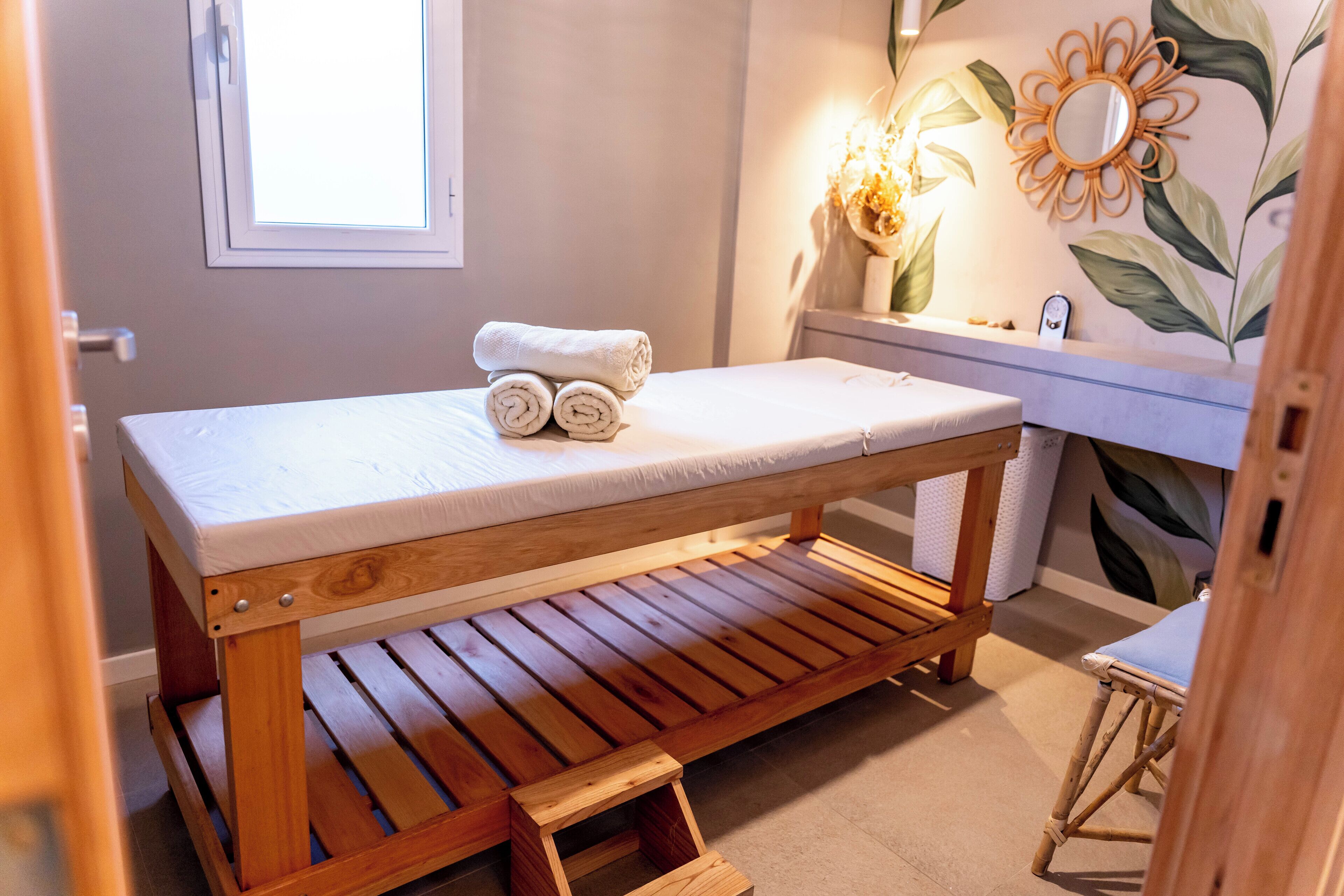 A wooden massage table with a white mattress, a wooden bench, and a small step stool.